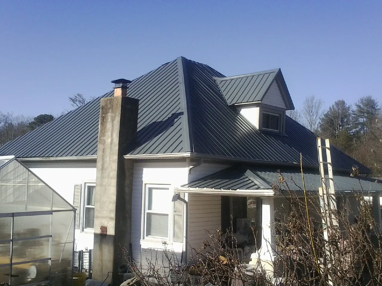 Dark blue standing seam metal roof on a white farmhouse with dormer — Slate & Tile Roof Repair by Roofing Brothers in Gooding