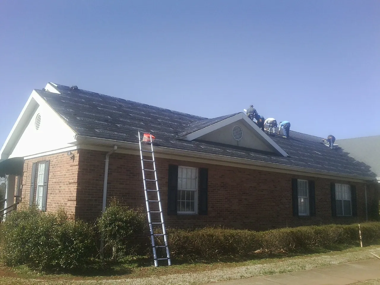 Crew tearing shingles off a brick ranch roof with a ladder set — Emergency Roof Repair work by our crew in Gooding