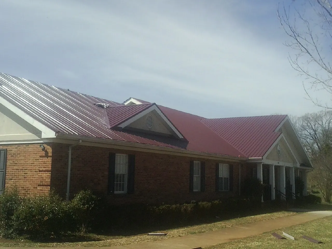 Red metal roof with gabled entries on a long brick building, from a Hail Damage Roof Repair job in Gooding