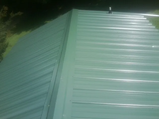 New green metal panels meeting at the ridge of a roof — Flat Roof Repair work by our crew in Gooding