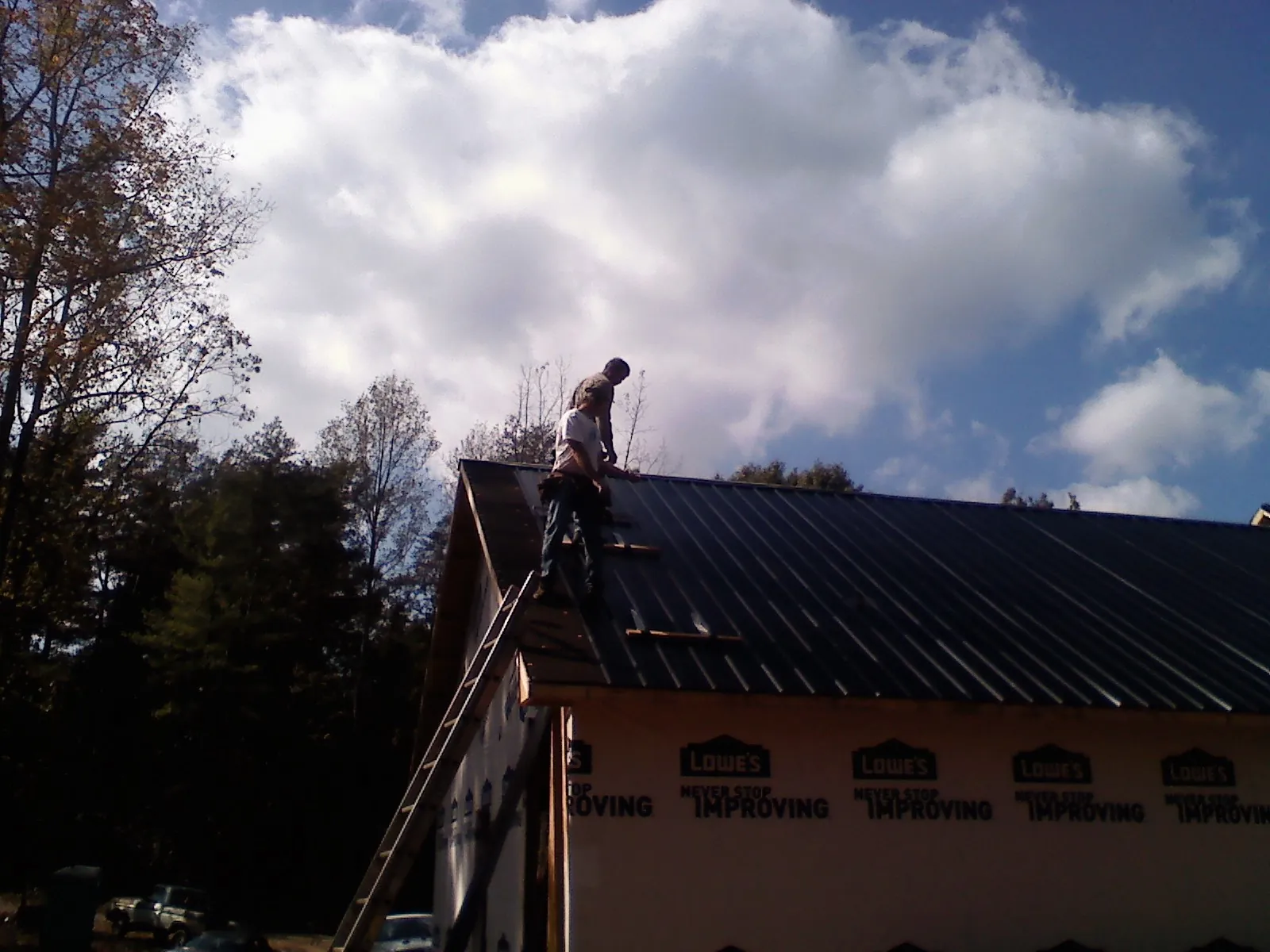 Roofer fastening dark metal panels high against a cloudy sky, from a Roof Inspection job in Gooding