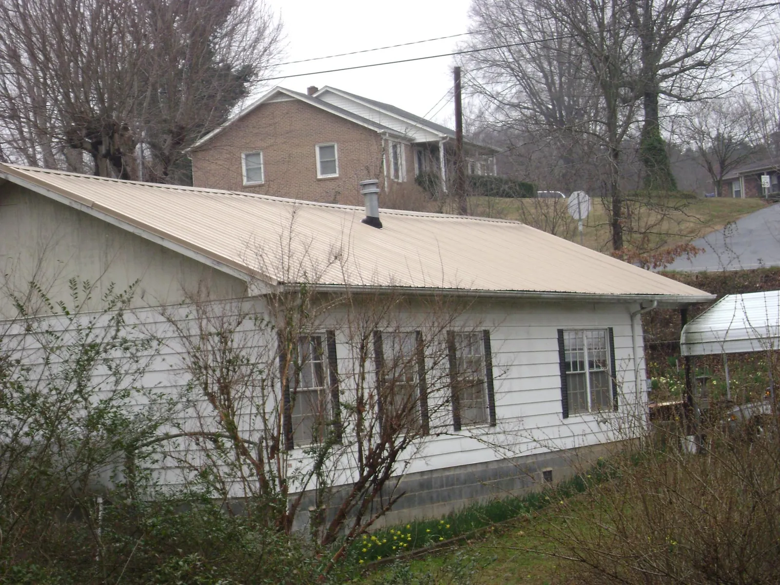 Tan metal roof on a white sided house set into a hillside — Commercial Roofing by Roofing Brothers in Gooding